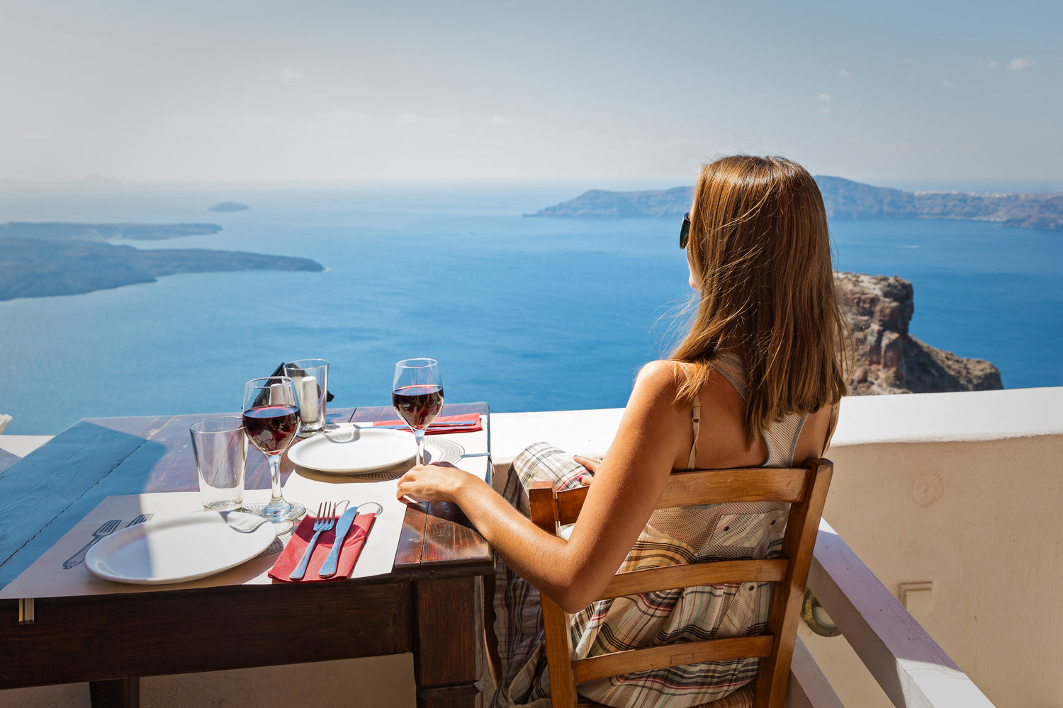 a woman admiring small islands from a patio while drinking red wine